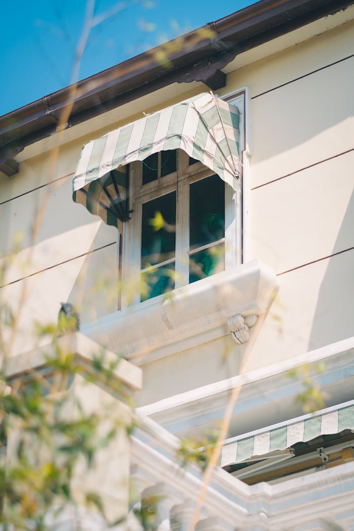 Elegant house window with striped awning and sunny ambiance, perfect for architectural themes.